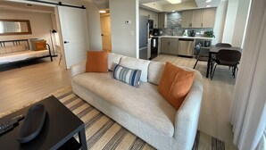 A modern living room with a sofa, a dining table, and a kitchen in the background.