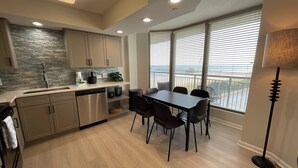 A modern kitchen with a dining area, large windows, and a view of the outdoors.