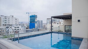 Une piscine sur le toit offrant une vue sur les bâtiments environnants et une grue de chantier.