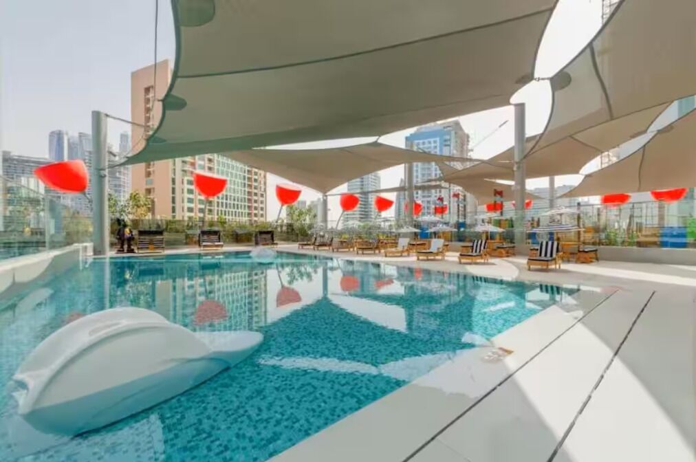 A swimming pool with lounge chairs and umbrellas, surrounded by modern buildings.