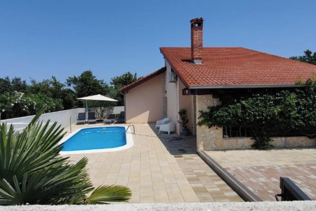 A house with a swimming pool, a tiled patio, and a red-tiled roof.