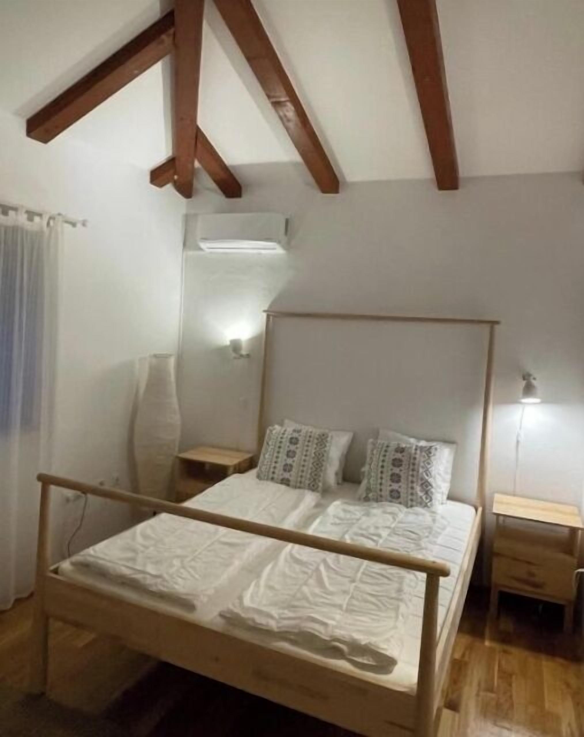 A bedroom with a wooden bed frame, two bedside tables, a mirror, and a wall-mounted air conditioner.