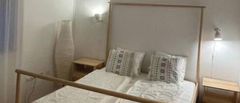A bedroom with a wooden bed frame, two bedside tables, a mirror, and a wall-mounted air conditioner.
