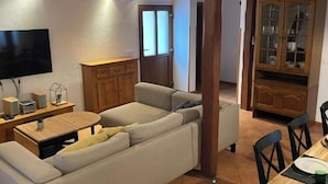 A living room with a sofa, wooden cabinet, TV, and a dining area with chairs and a table.