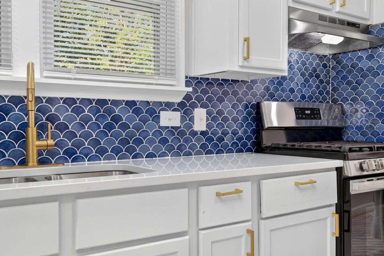 A kitchen with white cabinets, a blue tiled backsplash, a stainless steel range hood, and a gas stove.