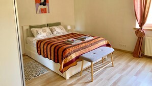 Een net opgemaakt bed met een geborduurd plaid, een bedlampje en een klein bankje.