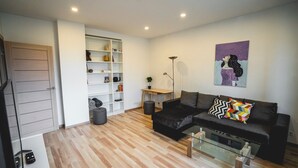 Een moderne woonkamer met een zwarte bank, een glazen salontafel en een witte boekenkast.