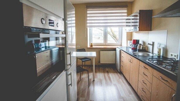 Een moderne keuken met een inbouwoven, een eettafel en een raam met jaloezieën.