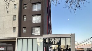 A modern building with a glass facade, a visible entrance, and a number '1796' on the side. - Oceana Suites Vicuña Mackena (Santiago)
