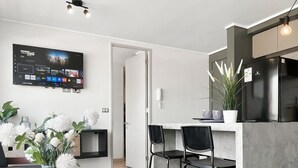 A modern kitchen with a built-in refrigerator, a dining area with bar stools, and a flat-screen TV mounted on the wall. - Oceana Suites Vicuña Mackena (Santiago)