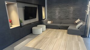 Ein modernes Wohnzimmer mit einem grauen Sofa, einem Flachbildfernseher, Holzboden und einer grauen Akzentwand.