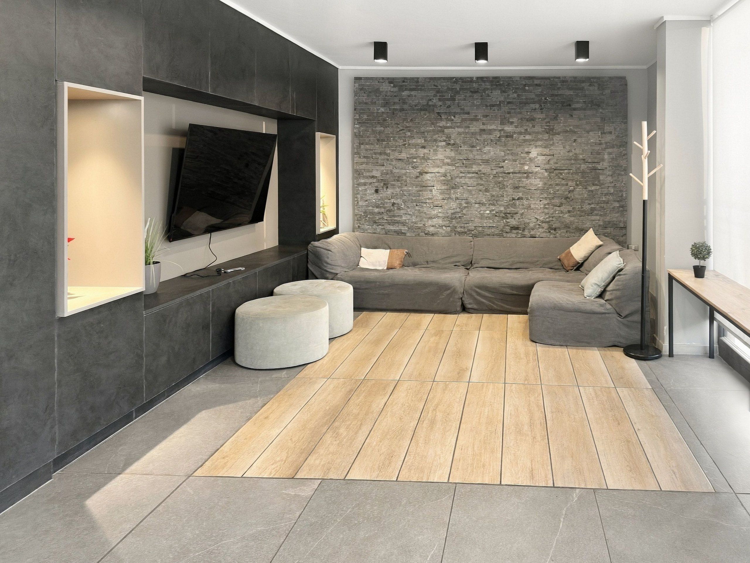 A modern living room with a sectional sofa, ottomans, a flat-screen TV, and a stone accent wall.