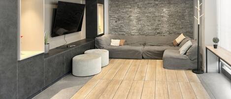 A modern living room with a sectional sofa, ottomans, a flat-screen TV, and a stone accent wall.