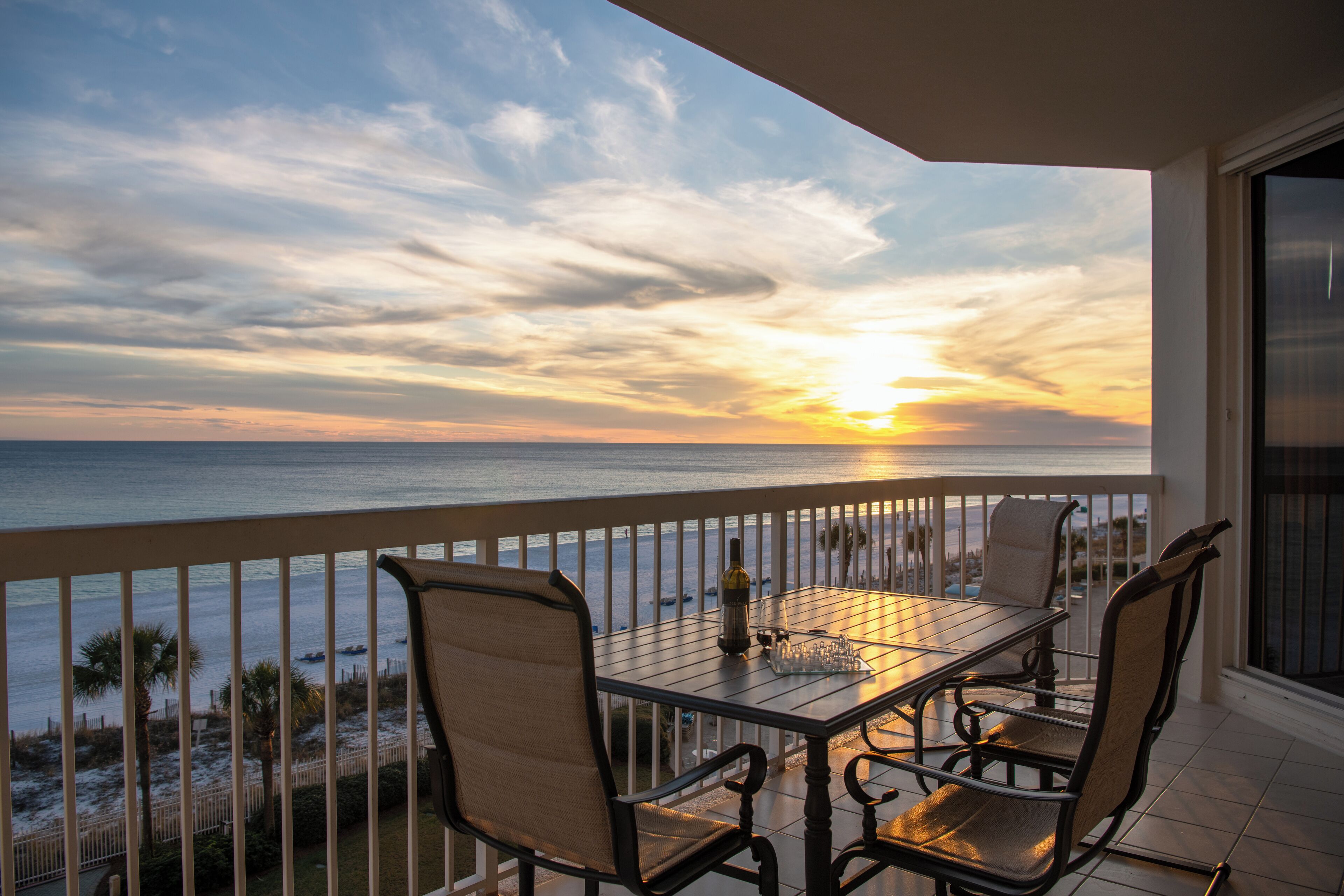 Varanda com mesa e cadeiras com vista para o oceano ao pôr do sol.