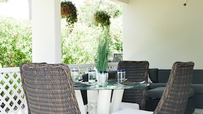 A glass-top table with wicker chairs, a white cushioned sofa, and hanging planters. - Lillian in Old Chancery Lane - 2BR Retreat Near Oistins, Long Beach, and Surfing (Christ Church)