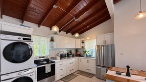 Una cocina moderna con armarios blancos, electrodomésticos de acero inoxidable y techo de madera.