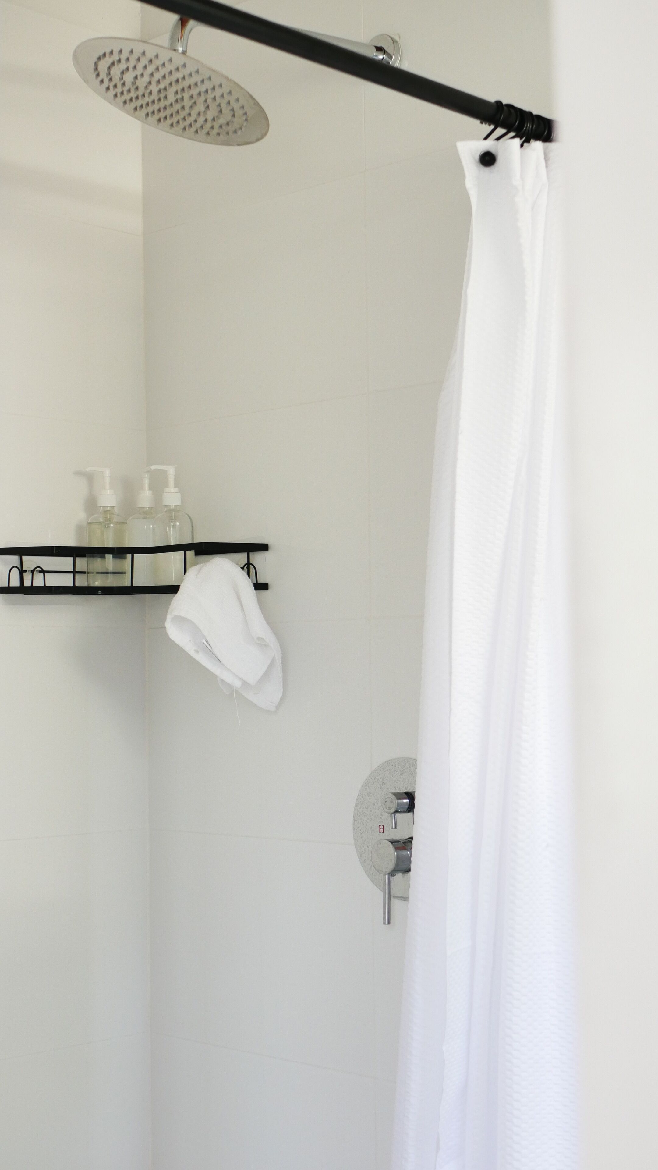 A modern bathroom with a shower, a towel rack, and a shelf with toiletries.