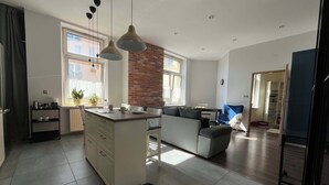A modern kitchen with a central island, a dining area with a sofa, and a view of the city through large windows.