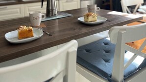 A modern kitchen with white cabinets, a coffee station, and a dining area with a wooden table and white chairs.