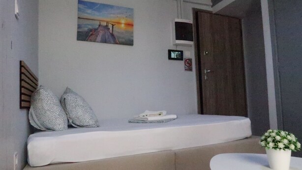 A room with a bed, a small table with a plant, a painting on the wall, and a door with a sign.