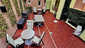 A rooftop terrace with a red tiled floor, a round table with chairs, and a grill.