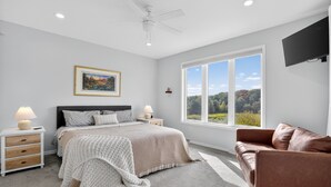 A bedroom with a bed, nightstands, a lamp, a television, and a large window with a view of trees. - Peaceful Secluded Wausau Retreat 3 Bedroom Home (Wausau)