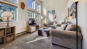 Ein geräumiges Wohnzimmer mit großem Fenster, einem Flachbildfernseher, einer Couch und einem Couchtisch.