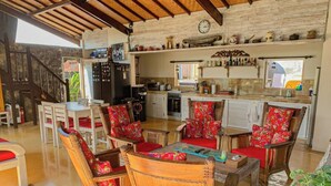 A spacious living area with wicker furniture, a kitchen in the background, and a rustic stone wall.