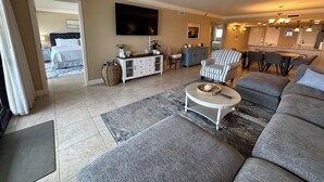 Un salon spacieux avec un grand canapé, une table basse, un fauteuil à rayures et un téléviseur fixé au mur.