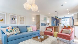 A modern living room with a blue sofa, a pink armchair, and a kitchen in the background. - Luxe Group Stay With Hot Tub Rooftop Lounge (Nashville)