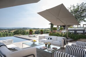 A sunlit outdoor seating area with a pool, lounge chairs, and a view of the countryside. - Il Mandorlo by Boutique (San Quirico d'Orcia)