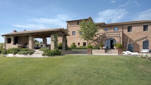 A large, multi-story brick house with a covered patio and a well-maintained lawn. - Il Mandorlo by Boutique (San Quirico d'Orcia)