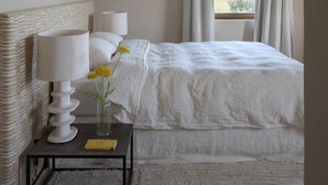 A bedroom with a bed, two bedside lamps, a nightstand with a lamp, a vase with flowers, and a window with curtains. - Il Mandorlo by Boutique (San Quirico d'Orcia)