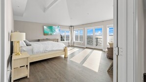 Un dormitorio amplio con una cama grande, un ventilador de techo y vistas a la playa a través de las ventanas.