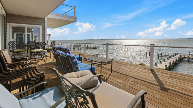 Una terraza de madera con mobiliario exterior, barandilla y vista al agua.
