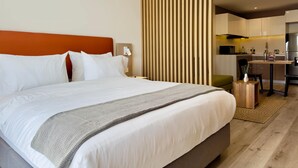 A modern hotel room with a large bed, a wooden partition, a small kitchen area, and a seating area. - w Sunlit Loft w Balcony in Santa Barbara (Bogotá)