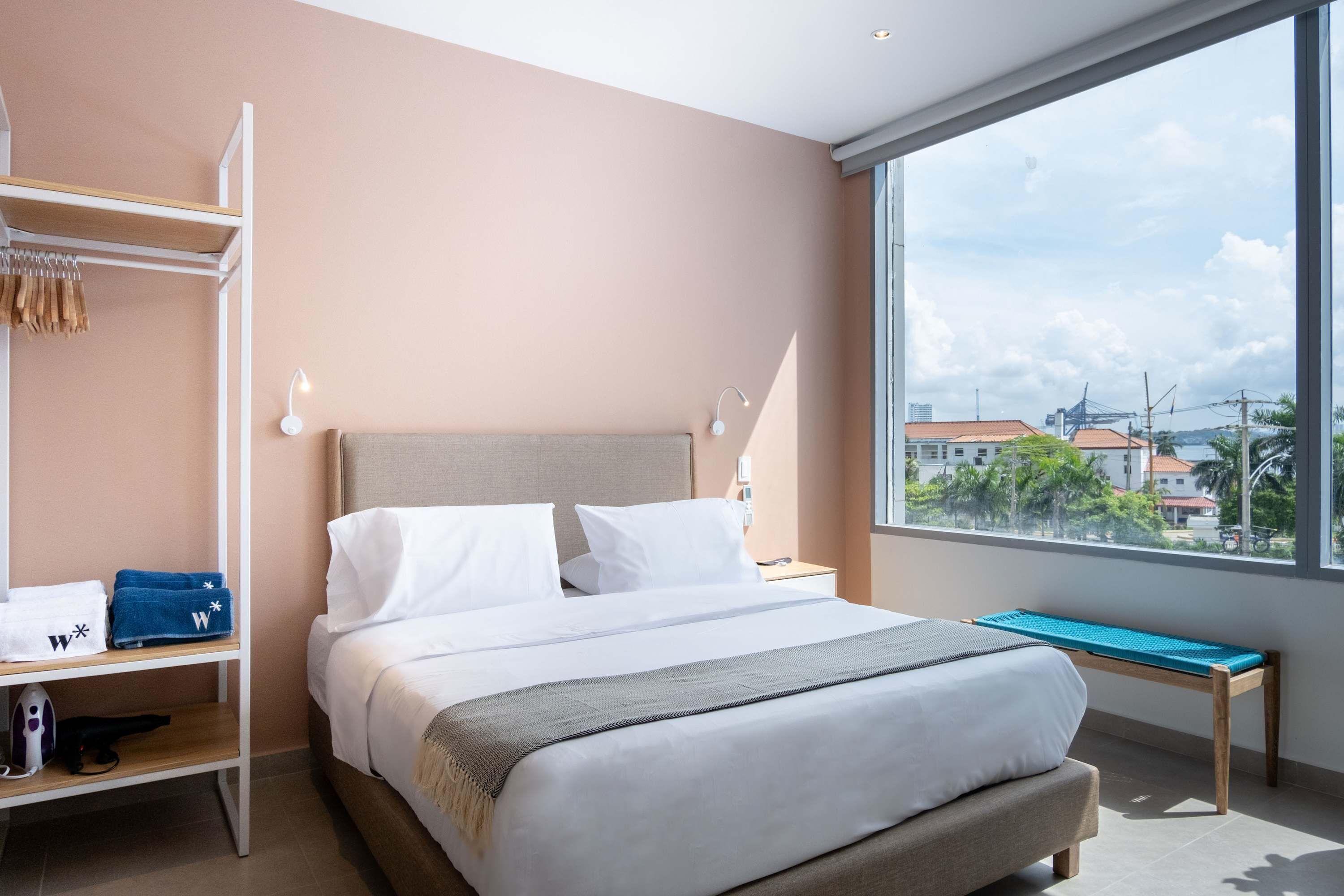 Moderni hotellihuone, jossa on suuri sänky, penkki, vaatekaappi ja näkymä kaupunkiin.