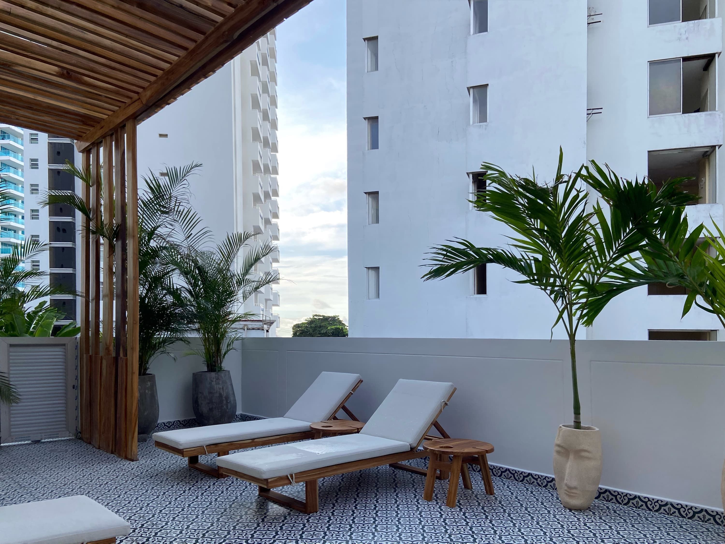 A rooftop terrace with two lounge chairs, a wooden table, and potted plants.