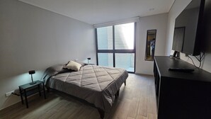 A bedroom with a bed, bedside tables, a desk, a mirror, and a TV. - Oceana Suites El Marquez (Santiago)
