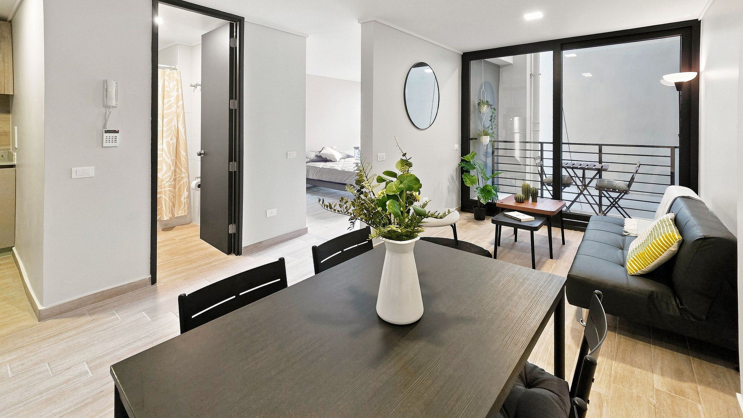 A modern living space with a dining area, a sofa, and a view of the outdoors.