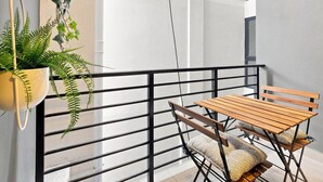 Un balcón con mesa y sillas de madera, una planta colgante y barandilla de metal negro.