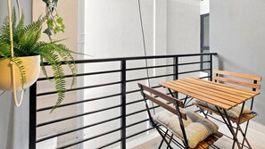Un balcón con mesa y sillas de madera, una planta colgante y barandilla de metal negro.