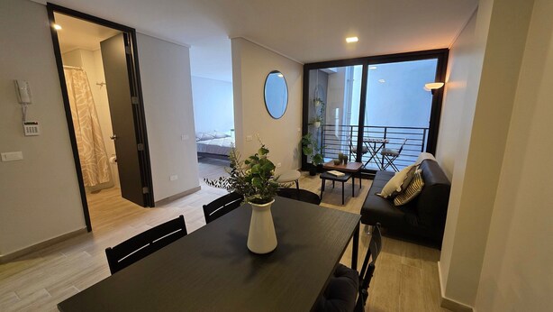 A modern living room with a dining table, a sofa, and a balcony with a view. - Oceana Suites El Marquez (Santiago)
