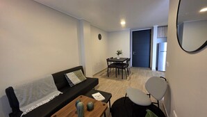 A living room with a sofa, a coffee table, a dining table with chairs, a small plant, and a door leading to another room. - Oceana Suites El Marquez (Santiago)