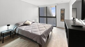 Un dormitorio moderno con cama, mesita de noche y escritorio con computadora.