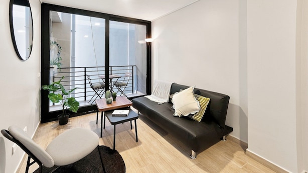 Una sala moderna con un sofá negro, una mesita, una silla y un balcón con barandilla.