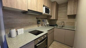A kitchen with wooden cabinets, a granite countertop, a microwave, a sink, and an oven. - Oceana Suites El Marquez (Santiago)