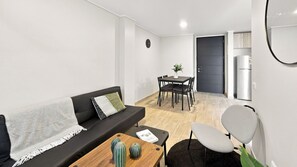 Un espacio habitable compacto con sofá, una mesa de comedor con sillas, una cocina con refrigerador y una pequeña mesa de centro.