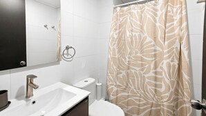 Un baño con lavamanos blanco, inodoro, espejo y cortina de ducha estampada con hojas.