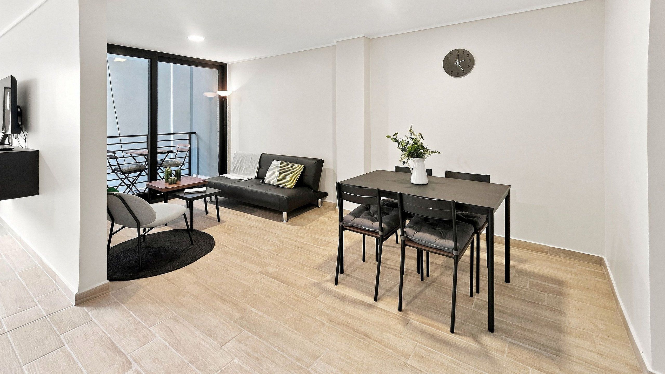 A modern living space with a dining area, a sofa, a coffee table, and a clock on the wall.